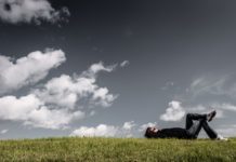 uomo sdraiato sul prato che guarda il cielo