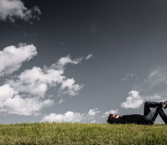 uomo sdraiato sul prato che guarda il cielo