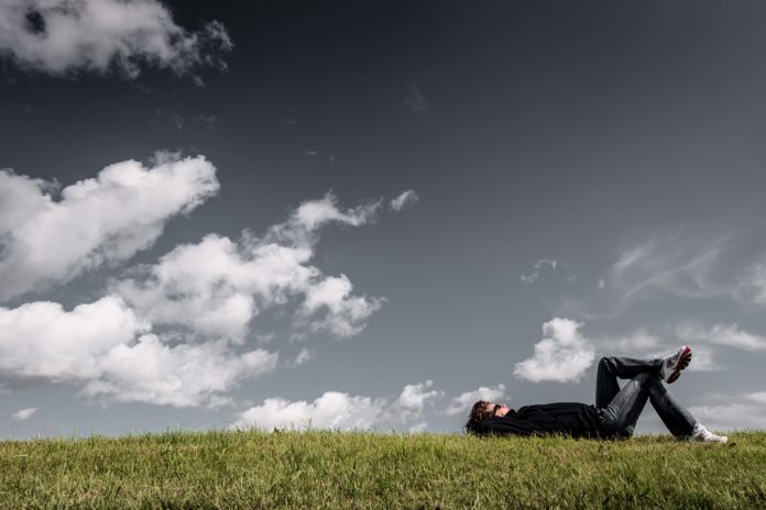 uomo sdraiato sul prato che guarda il cielo