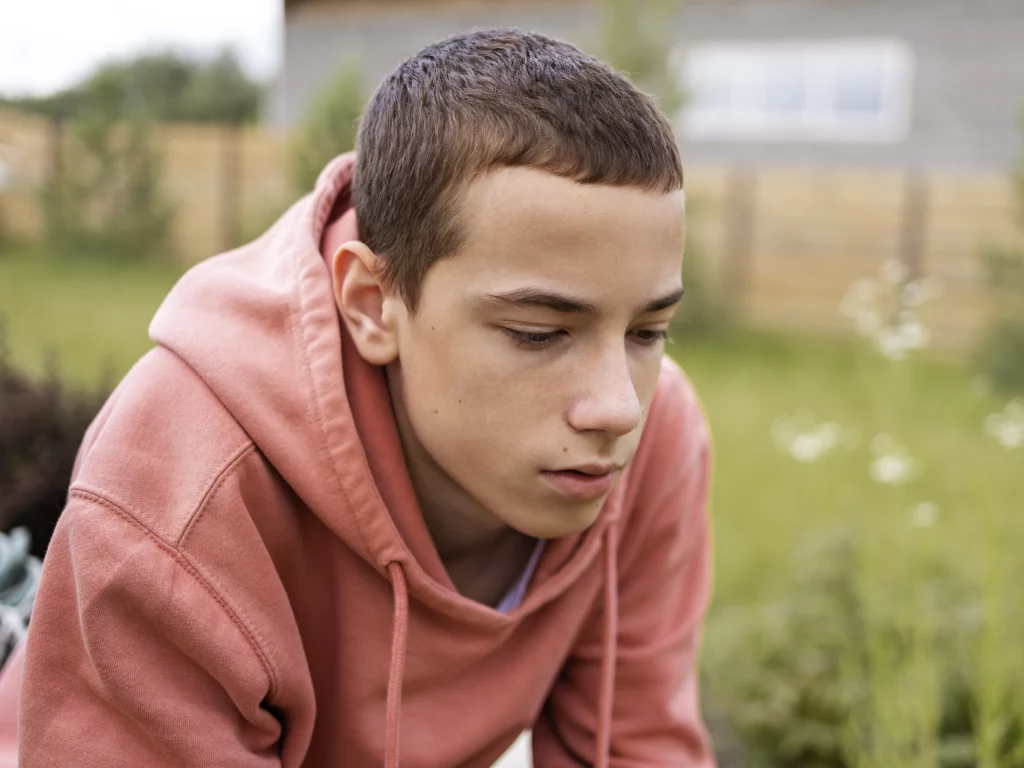 Ragazzo adolescente sorridente seduta su un prato verde durante una giornata di sole.