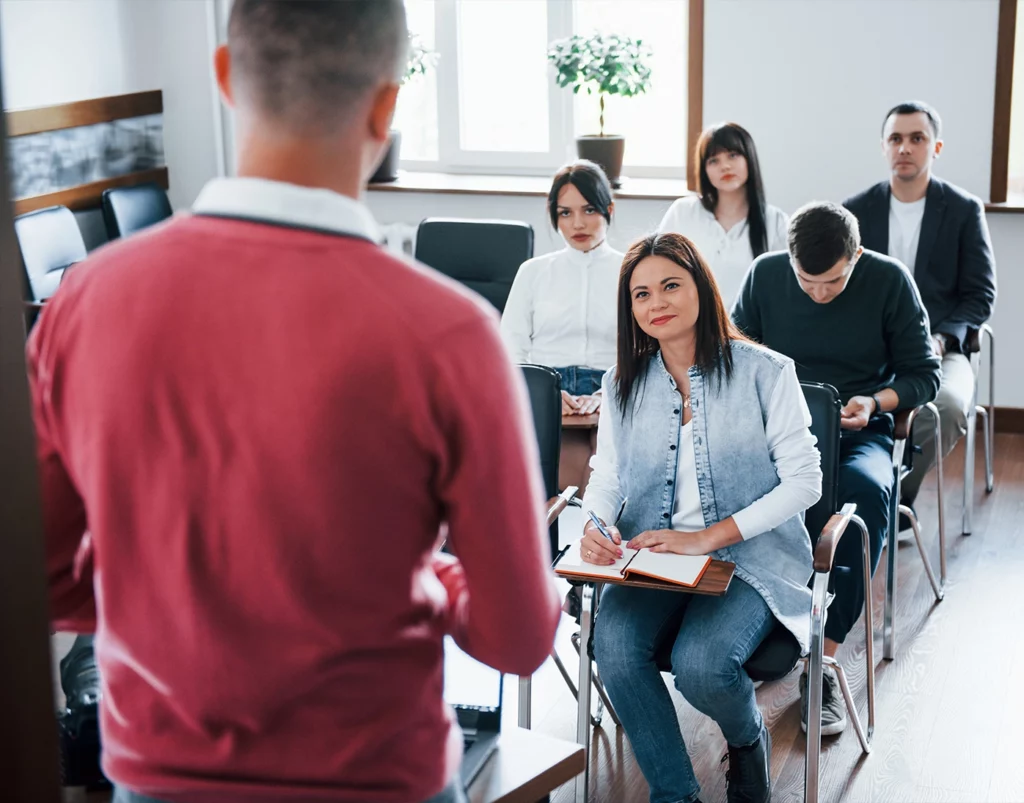 Docente che parla a un gruppo di persone in aula durante una lezione o un seminario formativo.
