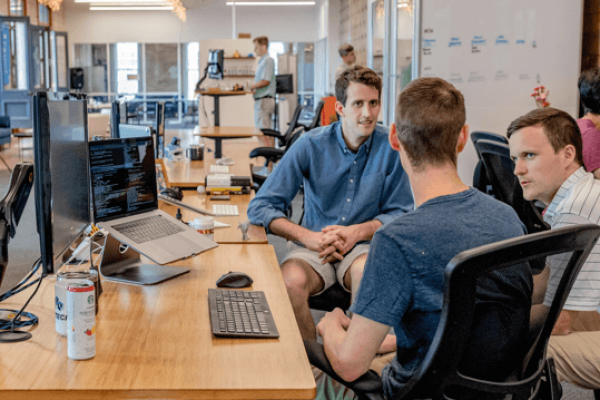 Gruppo di colleghi che discute in un ufficio open space moderno, simbolo di collaborazione e lavoro di squadra.