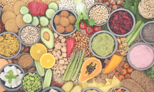 Tavolo con alimenti freschi e colorati: frutta, verdura, legumi e cereali disposti in ciotole.