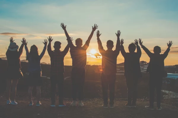 Gruppo di persone al tramonto con le braccia alzate, simbolo di unione, collaborazione e energia condivisa.