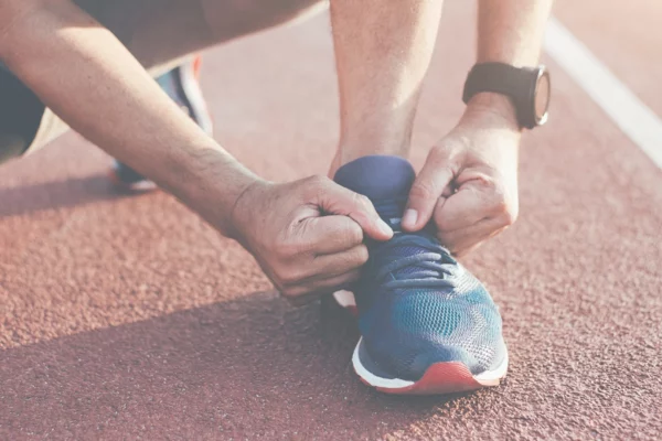 Persona che si allaccia le scarpe da corsa su una pista, simbolo di preparazione e determinazione.