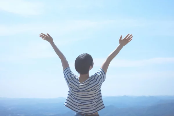 Persona di spalle con le braccia alzate verso il cielo, simbolo di libertà, fiducia e atteggiamento positivo.