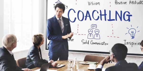 Formatore che presenta un progetto di coaching aziendale a un gruppo di colleghi in sala riunioni.