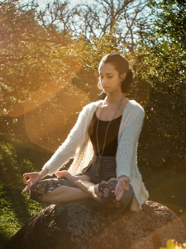 Donna che medita seduta su una roccia in un giardino illuminato dal sole, simbolo di calma e armonia interiore.