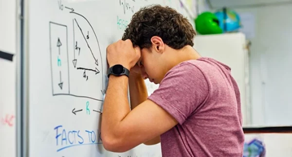 Ragazzo adolescente davanti a una lavagna scolastica, con espressione di difficoltà e incertezza.