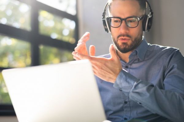 Uomo con cuffie che partecipa a un webinar online, parlando davanti al computer portatile.