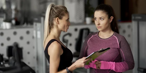 Coach che parla con una giovane donna in palestra, simbolo di ascolto, motivazione e supporto personalizzato.